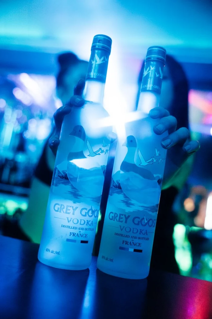 Dos botellas de vodka Grey Goose iluminadas, sostenidas sobre la barra bajo la luz azul