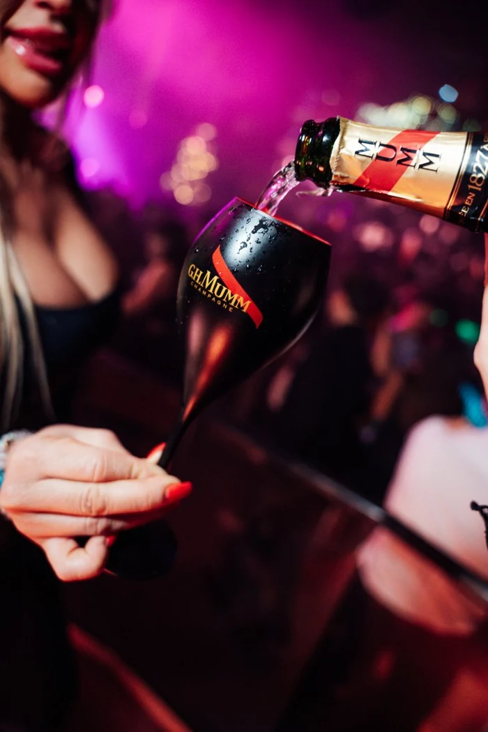 Una copa negra de G.H. Mumm servida junto a la pista, con las luces malvas de la sala detrás